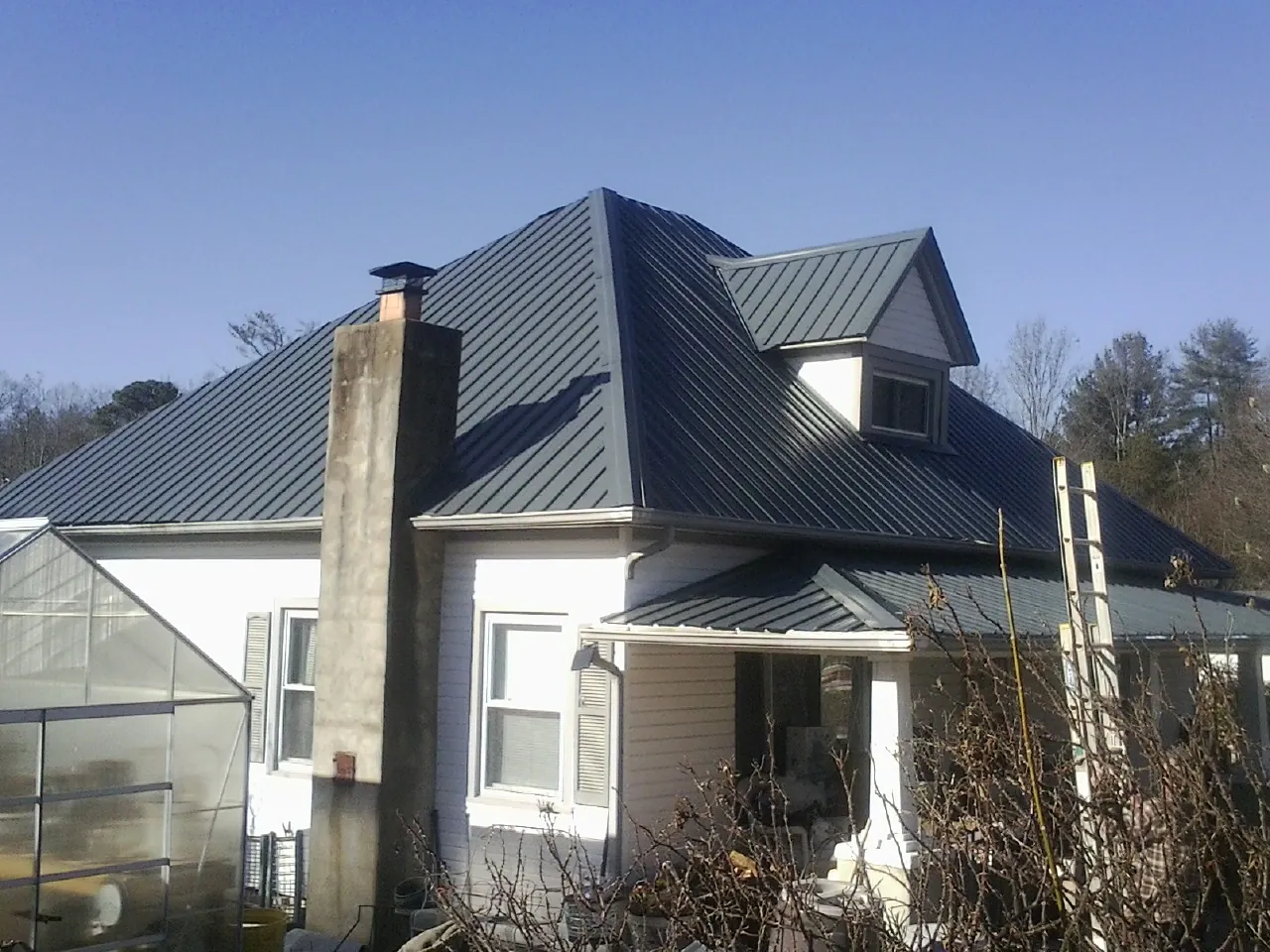 Dark blue standing seam metal roof on a white farmhouse with dormer — Slate & Tile Roof Repair by Roofing Brothers in Whitsett