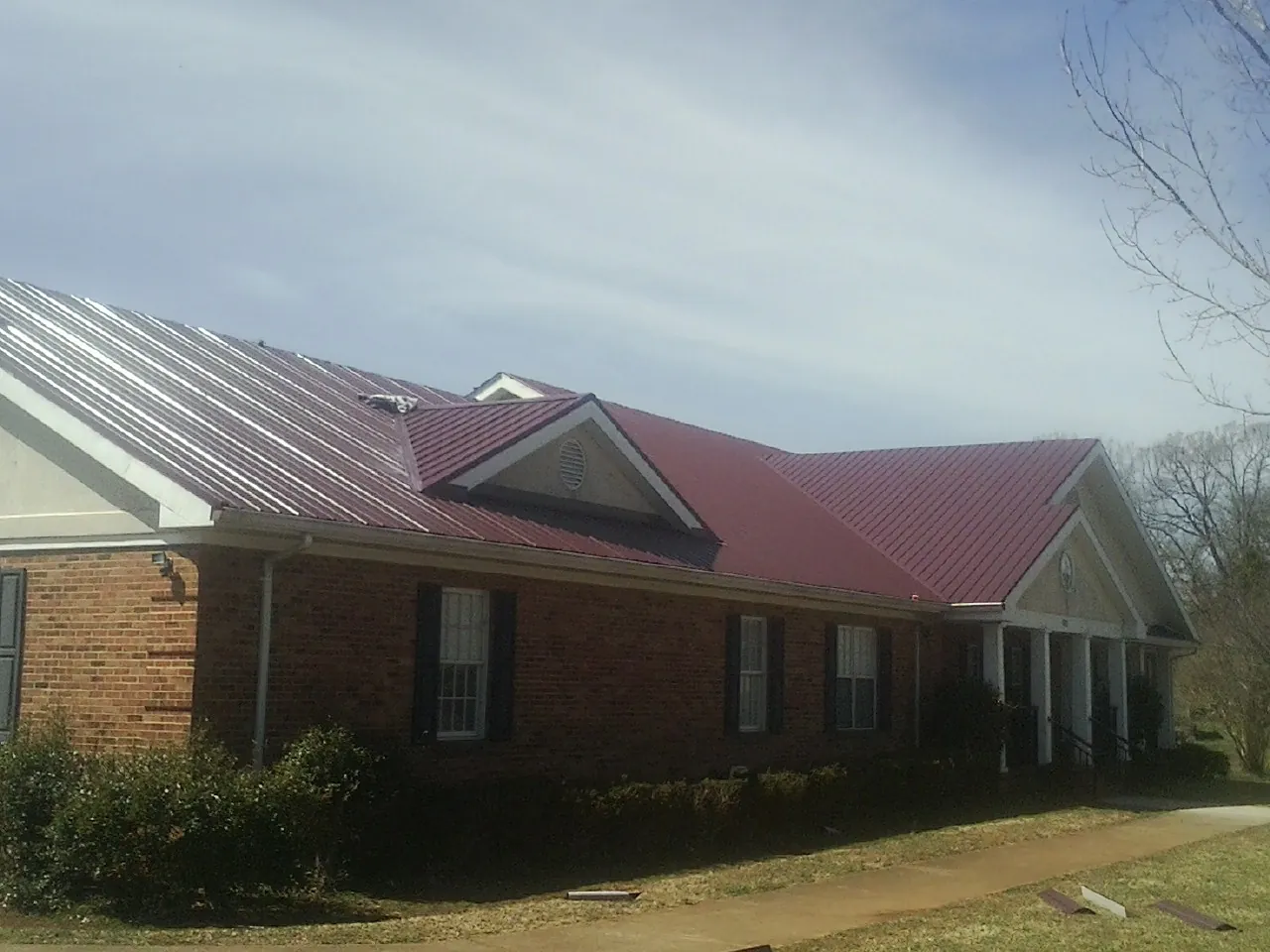 Red metal roof with gabled entries on a long brick building, from a Hail Damage Roof Repair job in Whitsett