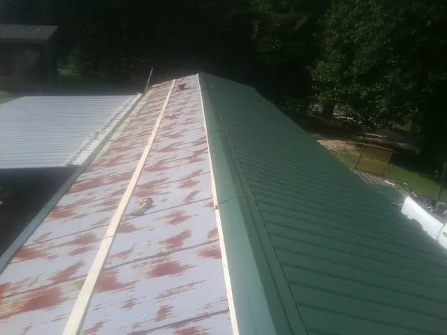Old rusted panels beside newly installed green metal roofing — Wind Damage Roof Repair by Roofing Brothers in Whitsett