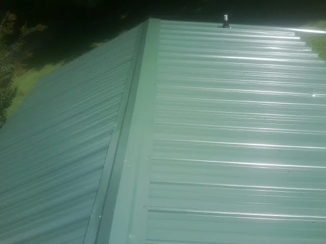 New green metal panels meeting at the ridge of a roof — Flat Roof Repair work by our crew in Whitsett