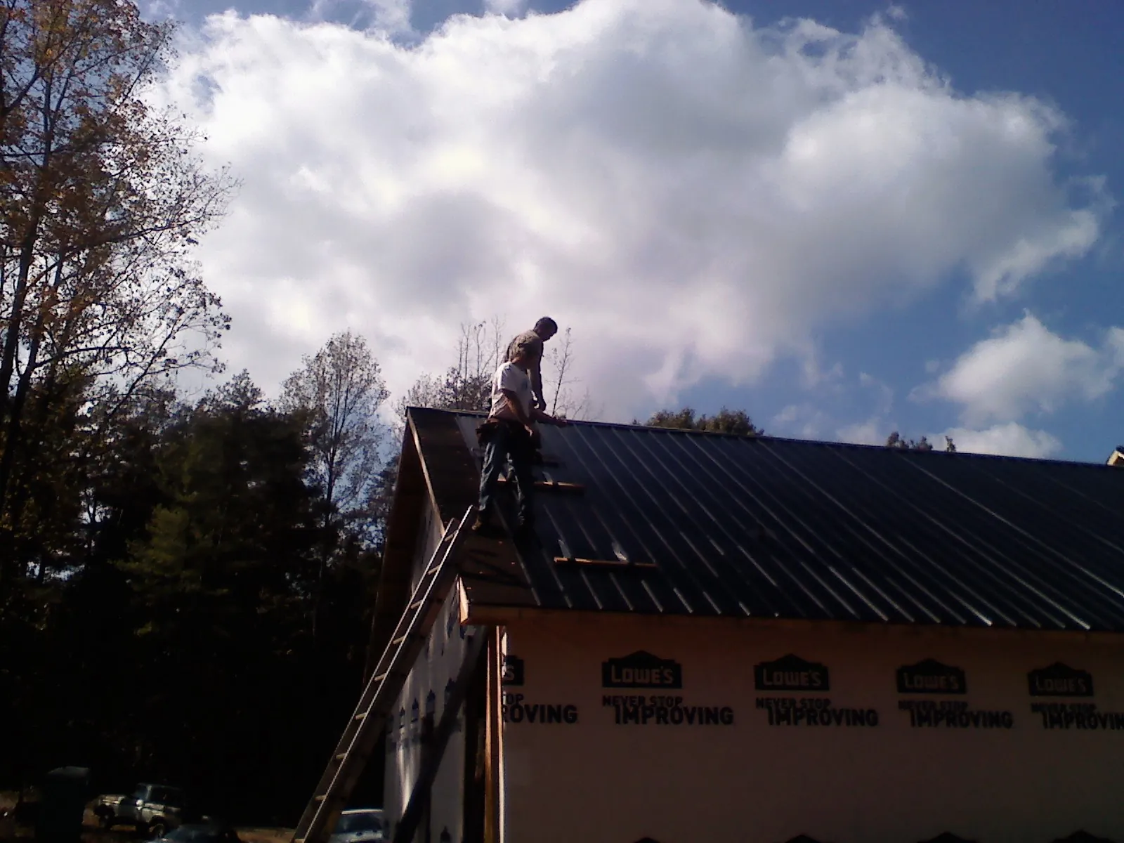 Roofer fastening dark metal panels high against a cloudy sky, from a Roof Inspection job in Whitsett