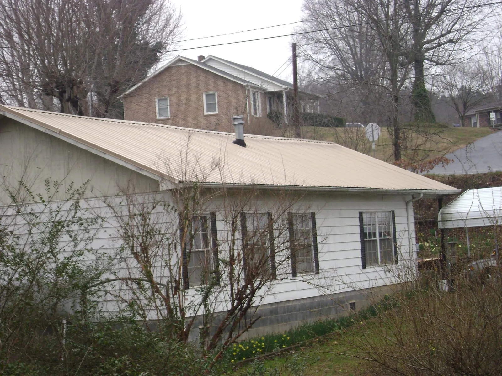 Tan metal roof on a white sided house set into a hillside — Commercial Roofing by Roofing Brothers in Whitsett