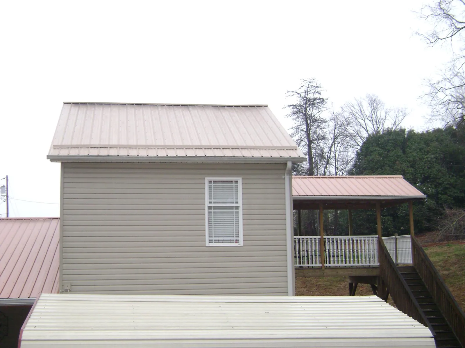 Tan metal roofs on a two story addition and attached porch, from a Roof Replacement job in Whitsett