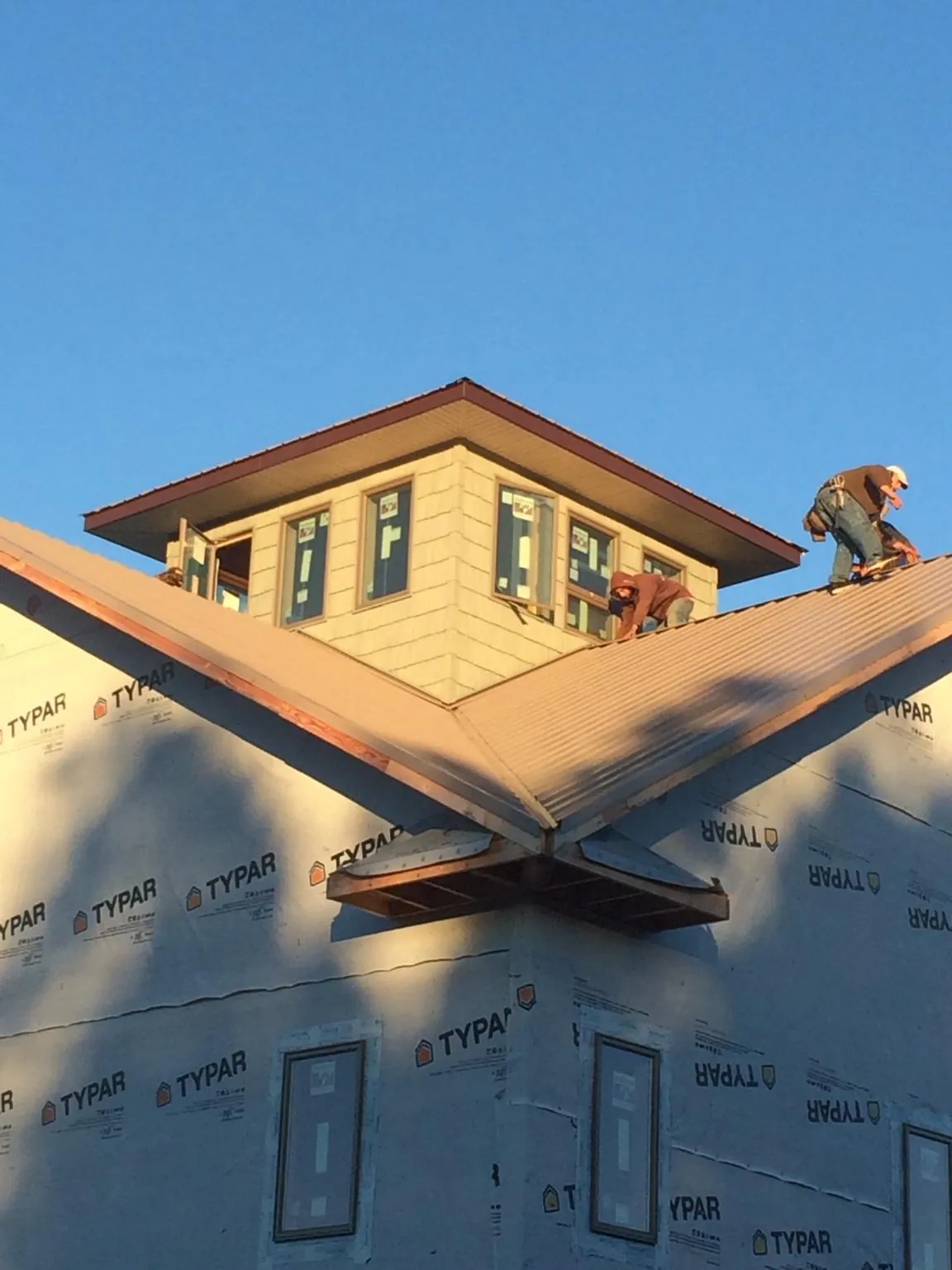 Roofers working around a rooftop cupola on a new metal roof at sunset — Roof Waterproofing in Whitsett by Roofing Brothers